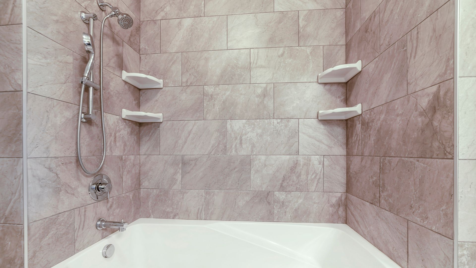 Pink-tiled bathroom shower and bathtub with wall shelves and handheld showerhead
