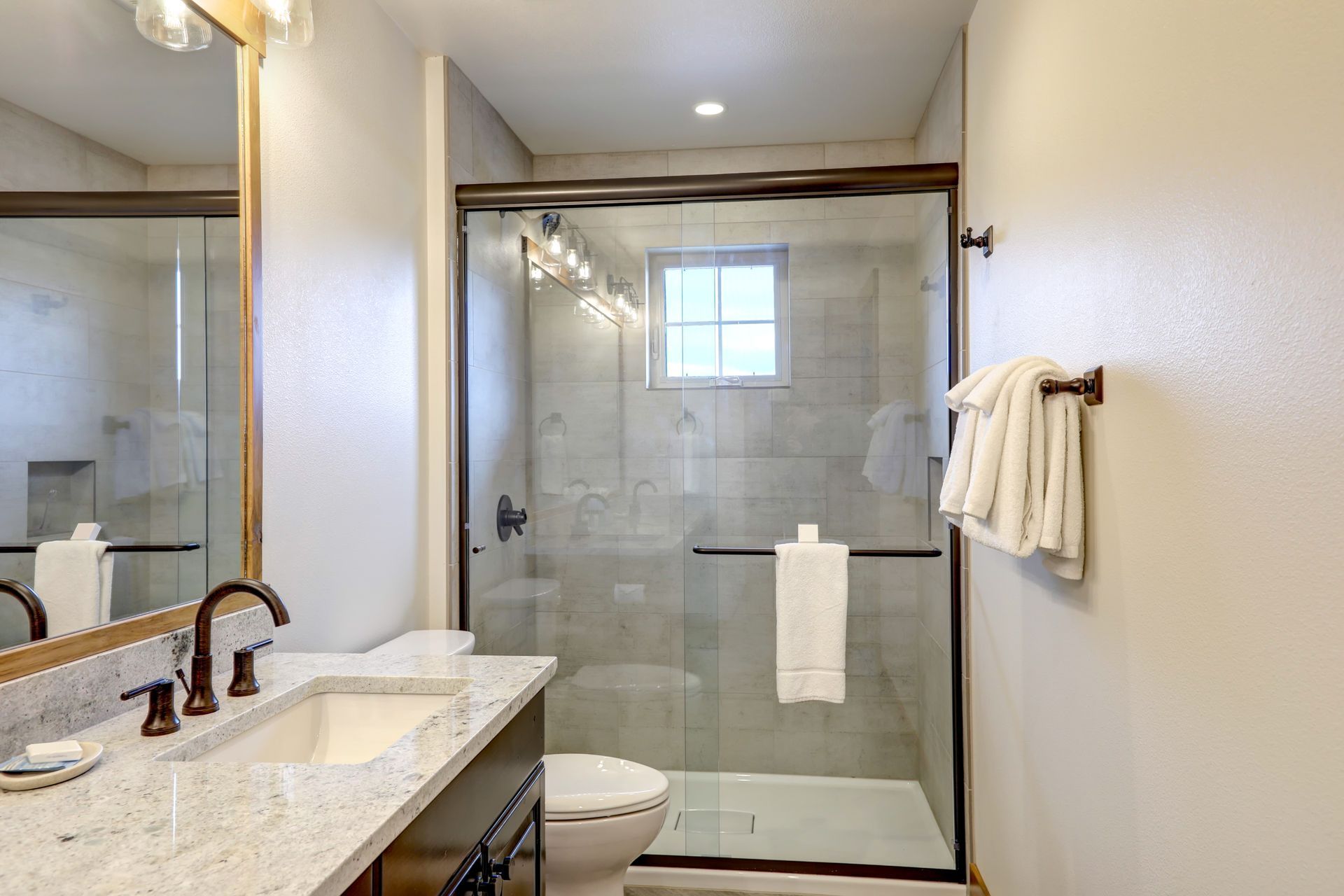 Bright bathroom with granite vanity, large mirror, and glass-enclosed shower with towel rack.