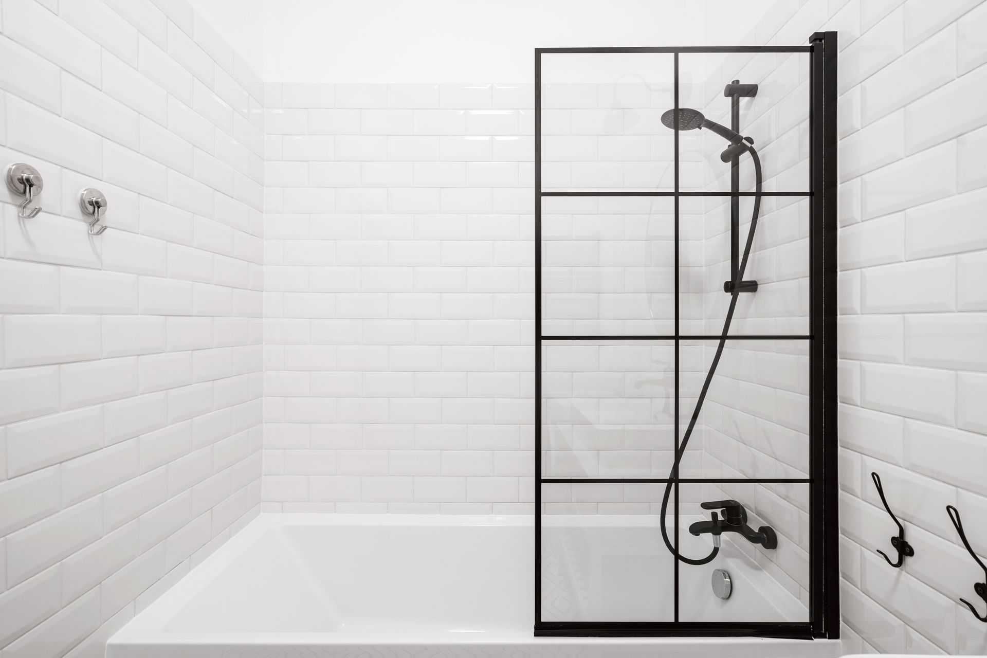 Minimal white bathroom with a bathtub and black-framed glass shower screen.
