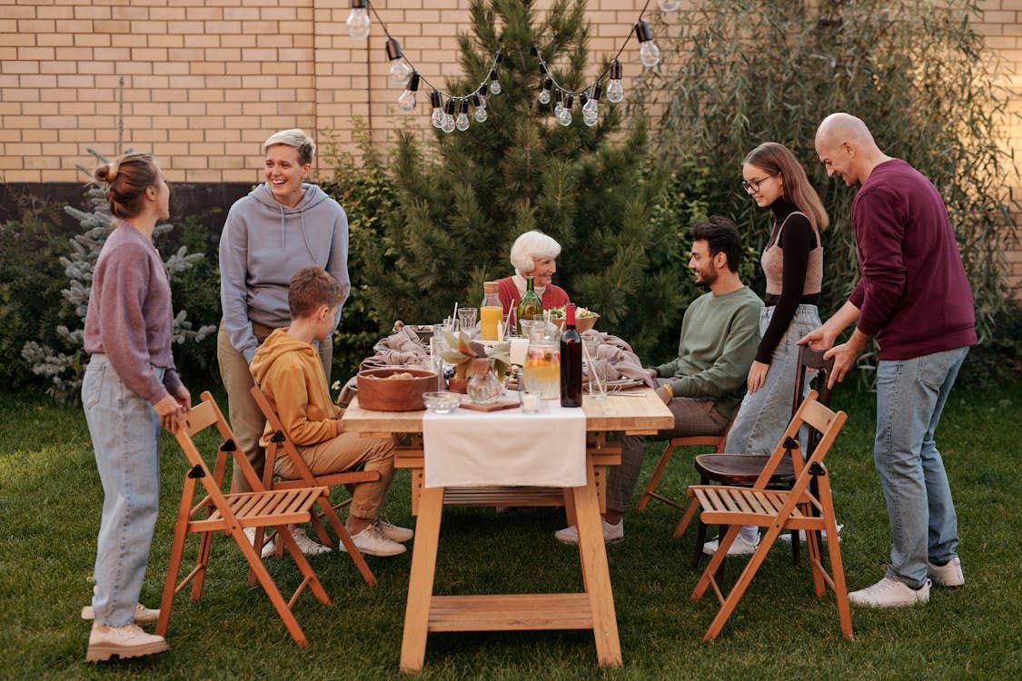 Family gathered around a wooden table in a backyard, preparing for a meal.