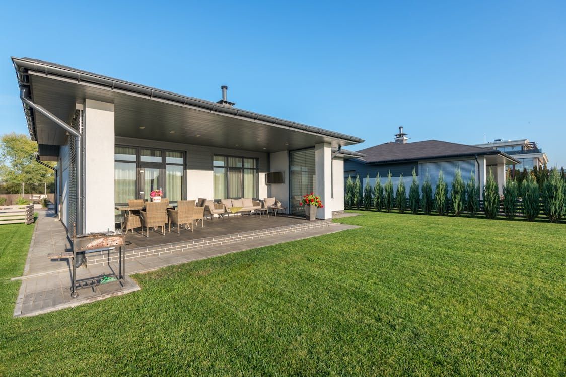 Modern house with covered patio, outdoor dining set, and green lawn on a sunny day.