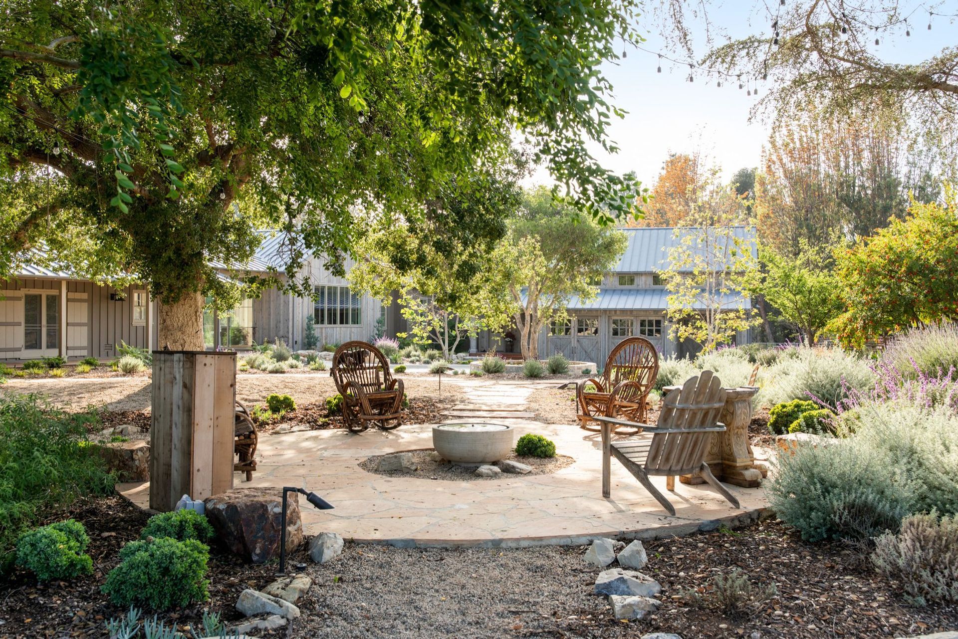 Outdoor seating area with chairs around a fire pit, next to a building and trees.