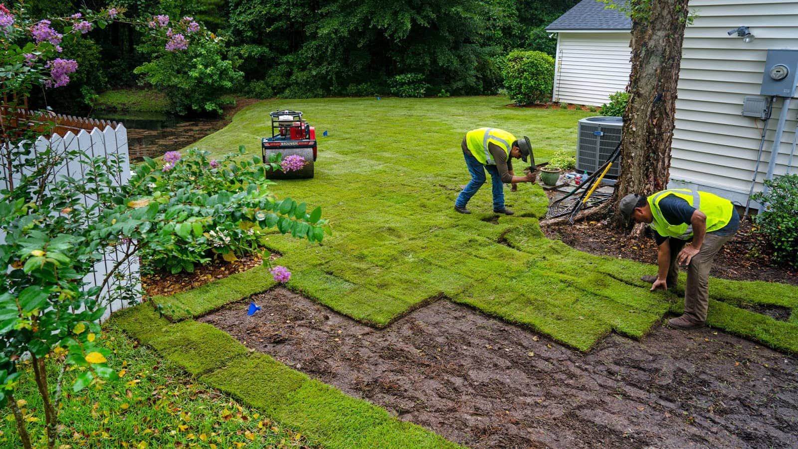 Lawn care workers install sod on a yard, using tools and wearing safety vests.
