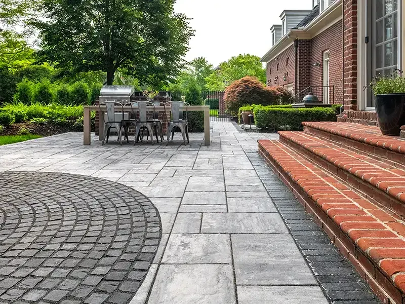 Patio with gray pavers, brick steps, dining table, and green landscaping. Patio with gray pavers, brick steps, dining table, and green landscaping.