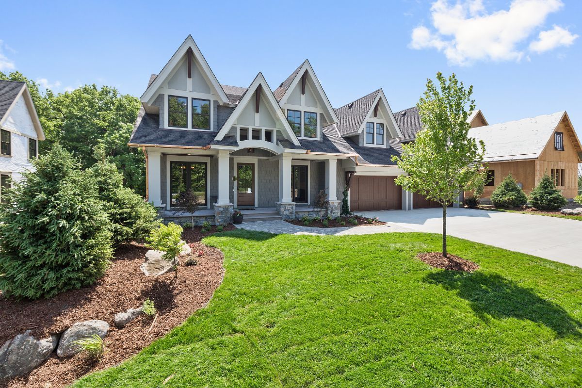 Gray and white house with multiple gables, lush green lawn, and blue sky.
