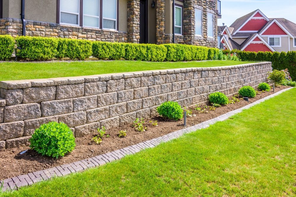 Stone retaining wall with green lawn, shrubs, and house in background. Stone retaining wall with green lawn, shrubs, and house in background.