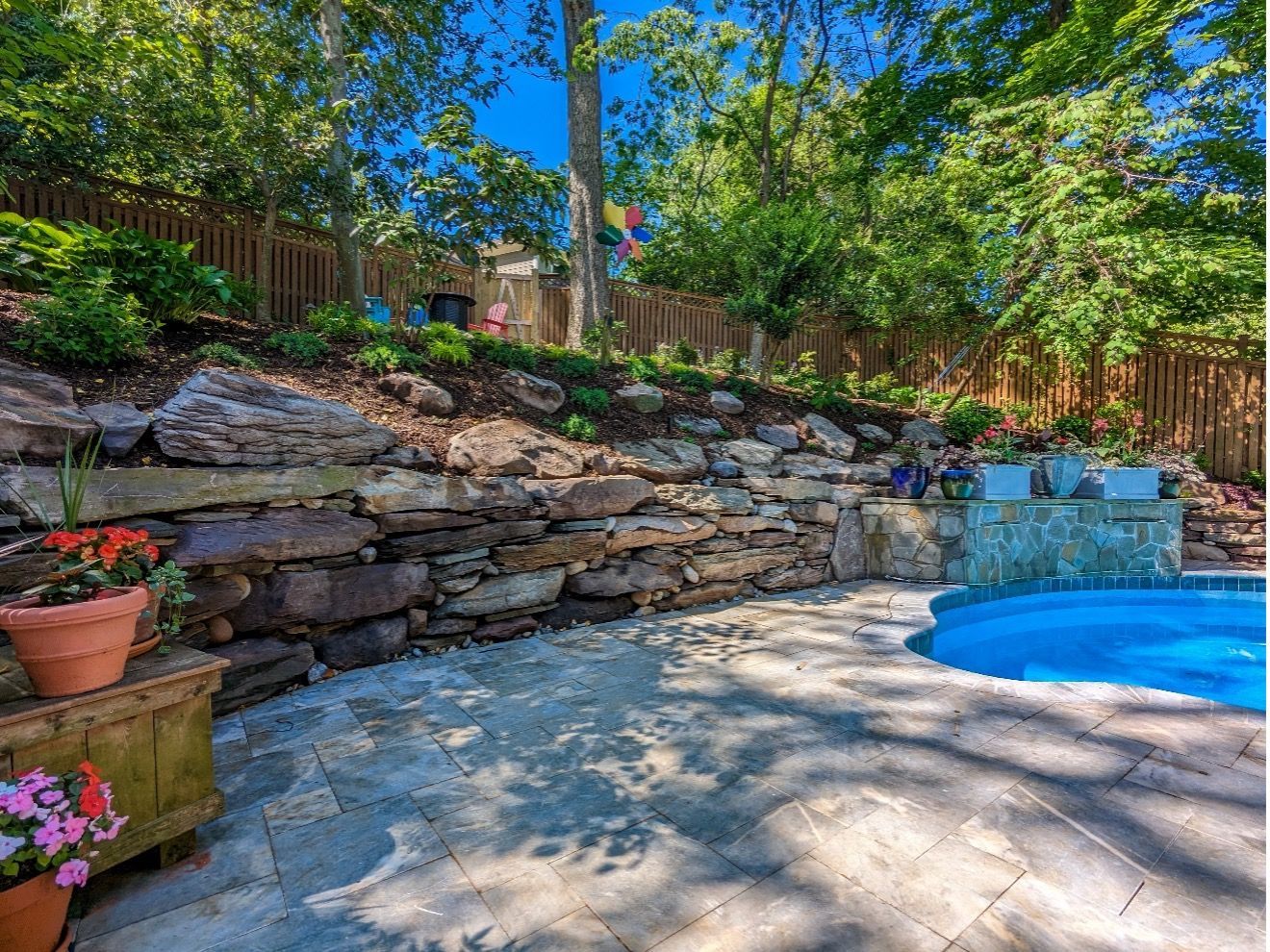 Stone retaining wall alongside a patio and pool with landscaping. Sunny day with blue sky. Stone retaining wall alongside a patio and pool with landscaping. Sunny day with blue sky.