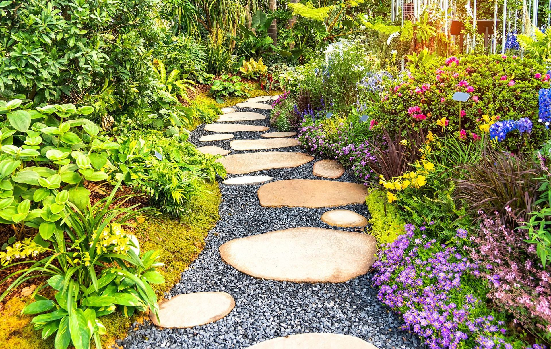 Stone path winds through a garden of colorful flowers and lush greenery.