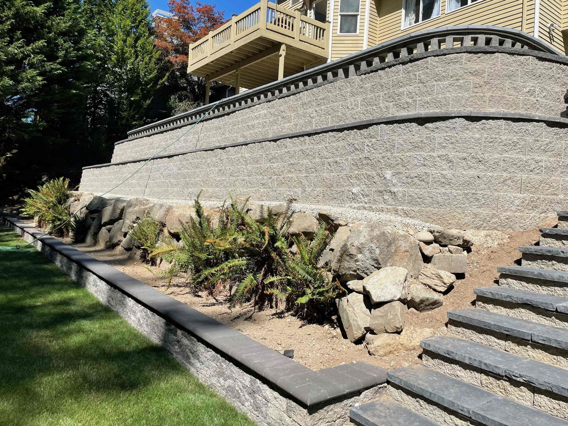 Stone retaining walls with steps leading up, plants along the front, and a house in the background. Stone retaining walls with steps leading up, plants along the front, and a house in the background.