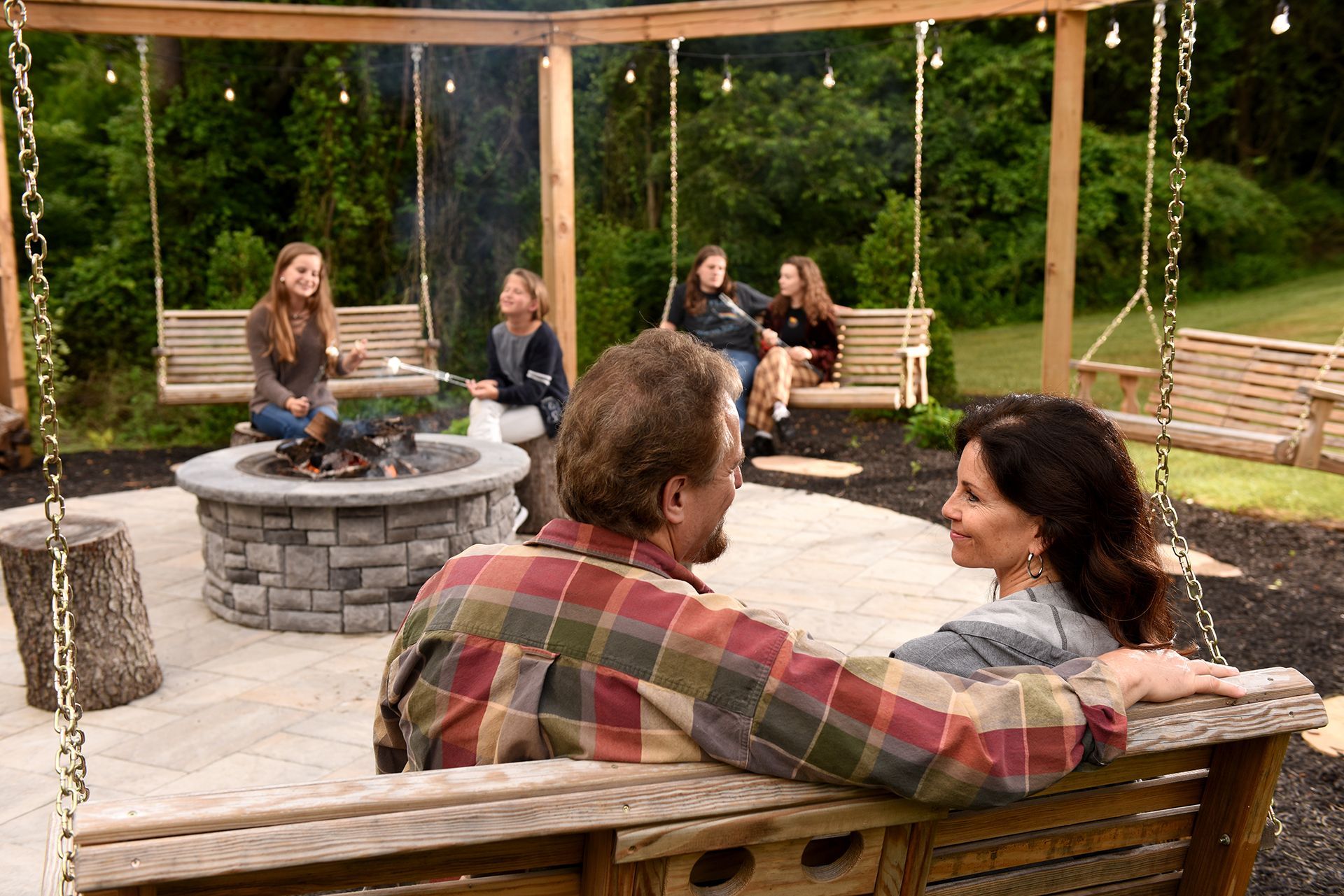Family gathering around a fire pit and swings in a backyard patio.