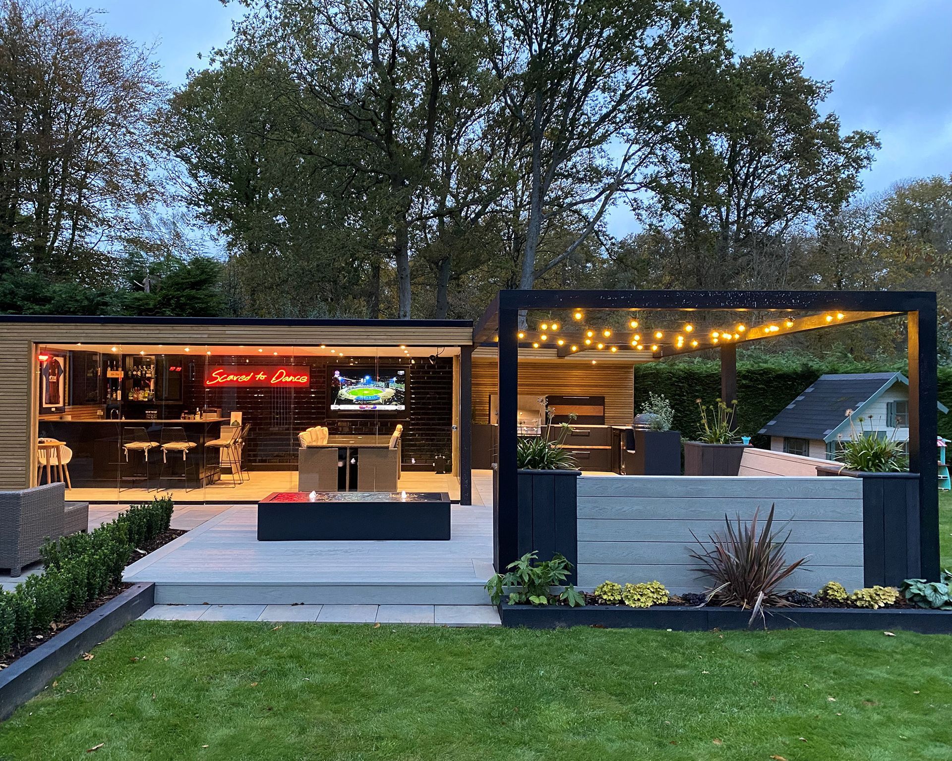Outdoor entertainment area with bar, seating, and fire pit under string lights.