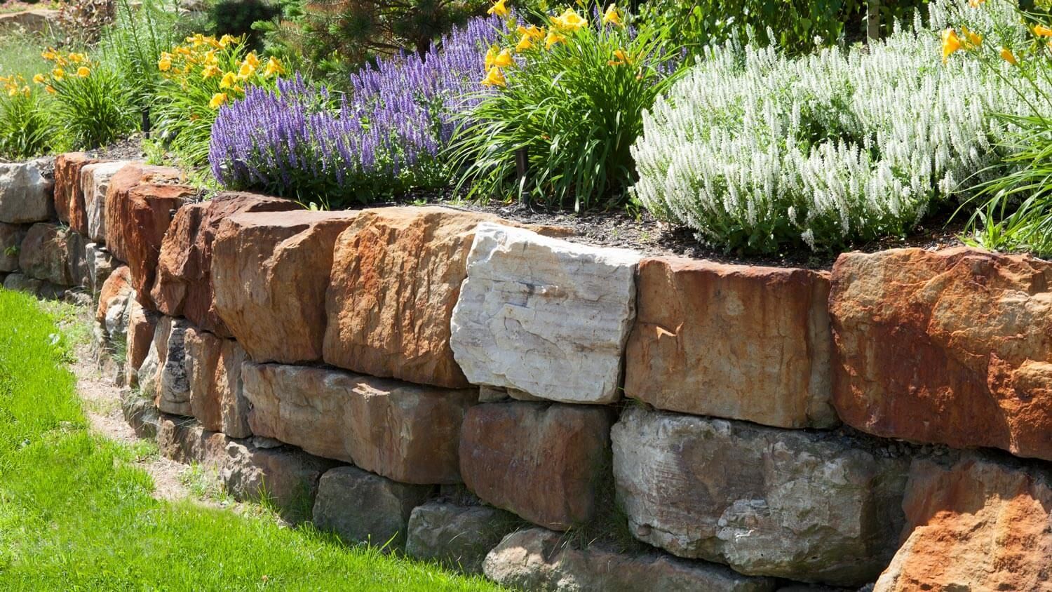 Stone retaining wall with colorful flowers in a garden.
