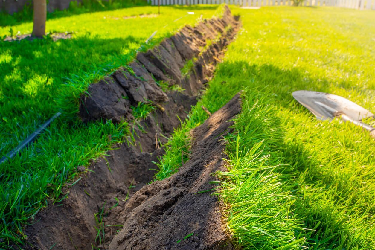A trench dug in a green lawn, with a shovel nearby.