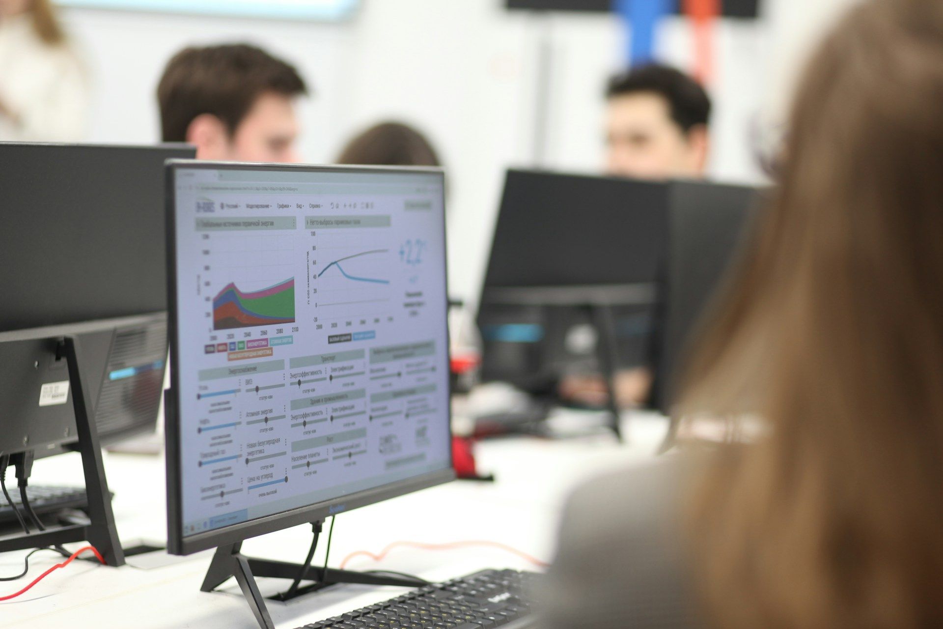 A woman is sitting in front of a computer monitor with dashboards displayed on it.