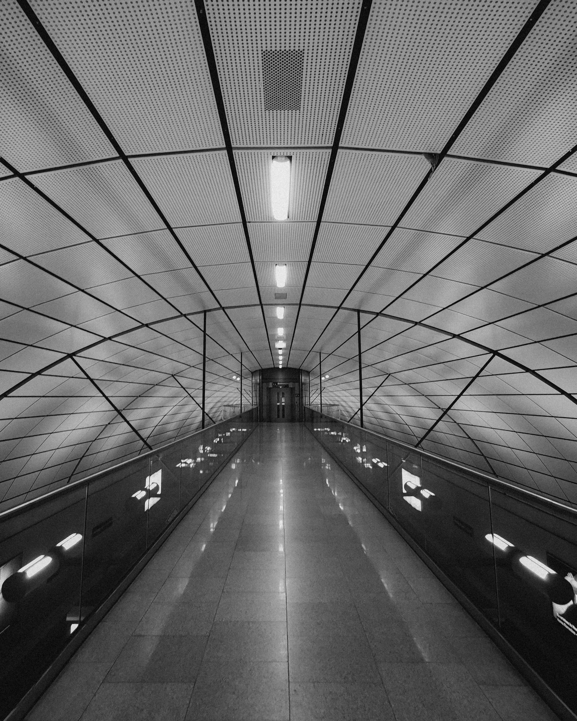 Black and white tunnel with geometric ceiling design, long walkway, and bright lights.