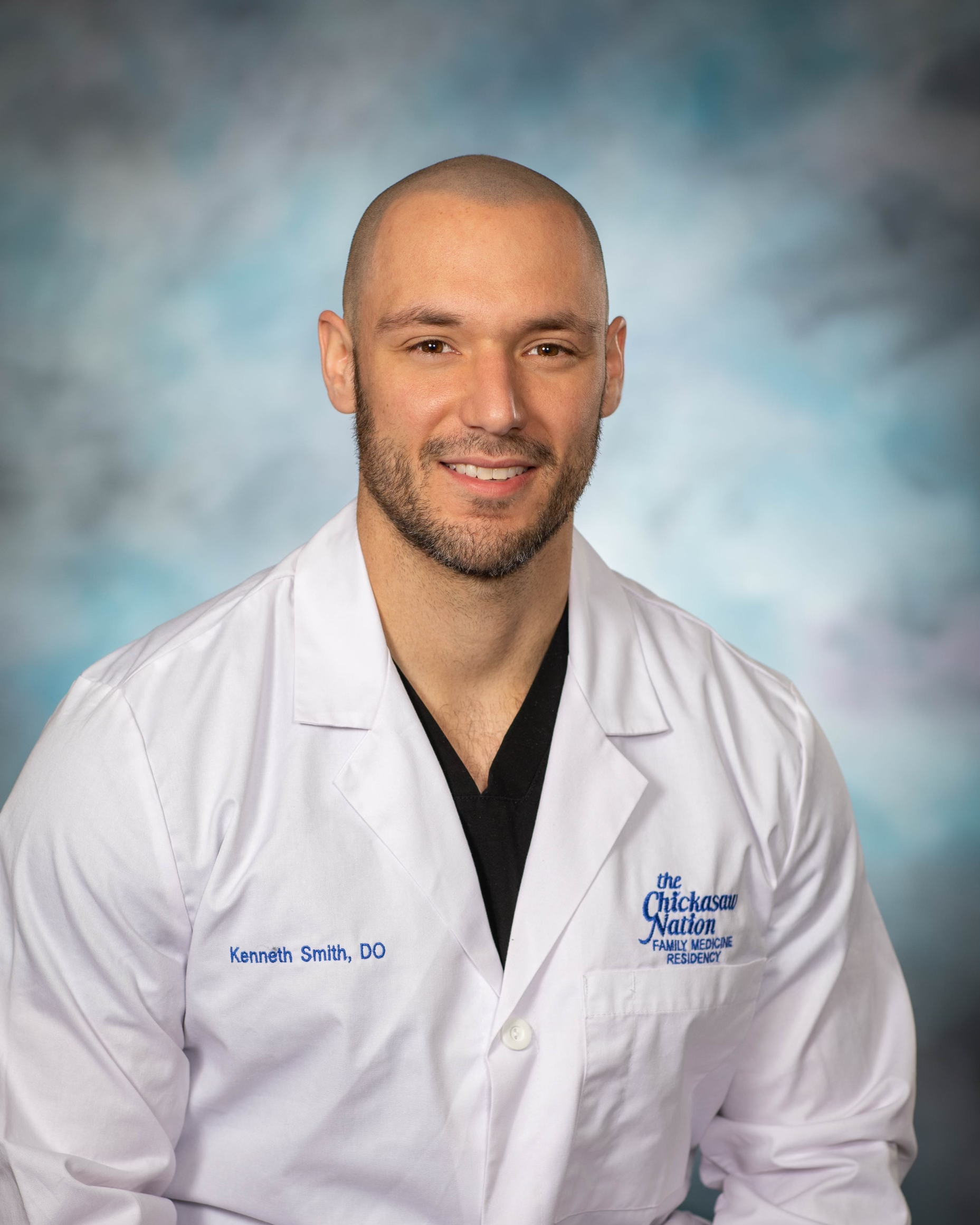 A man in a white lab coat is smiling for the camera