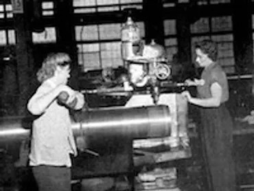 Two women are working on a machine in a factory.