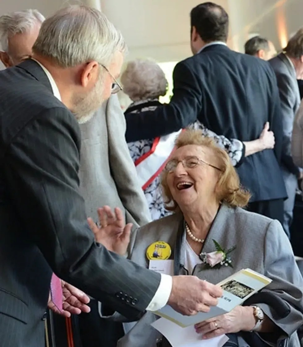 A woman in a wheelchair is laughing while talking to a man in a suit