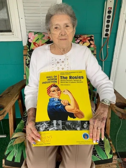 An elderly woman is holding a book titled the rosies