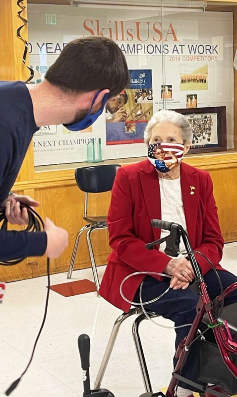 A man is taking a picture of an elderly woman wearing an american flag mask.