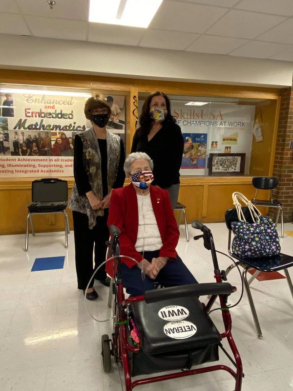 A woman in a wheelchair wearing a mask is standing next to two other women.
