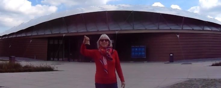 A woman in a red hoodie is standing in front of a large building.