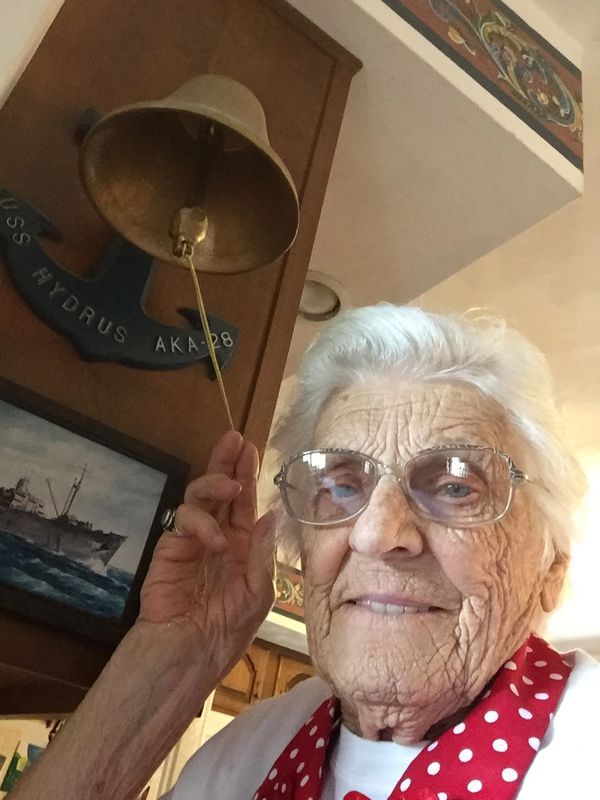 An elderly woman is holding a bell in front of a sign that says victory