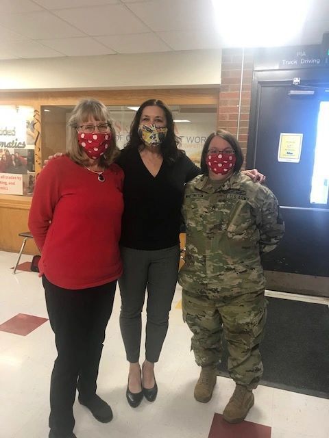 Three women wearing face masks are posing for a picture with a man in a military uniform.