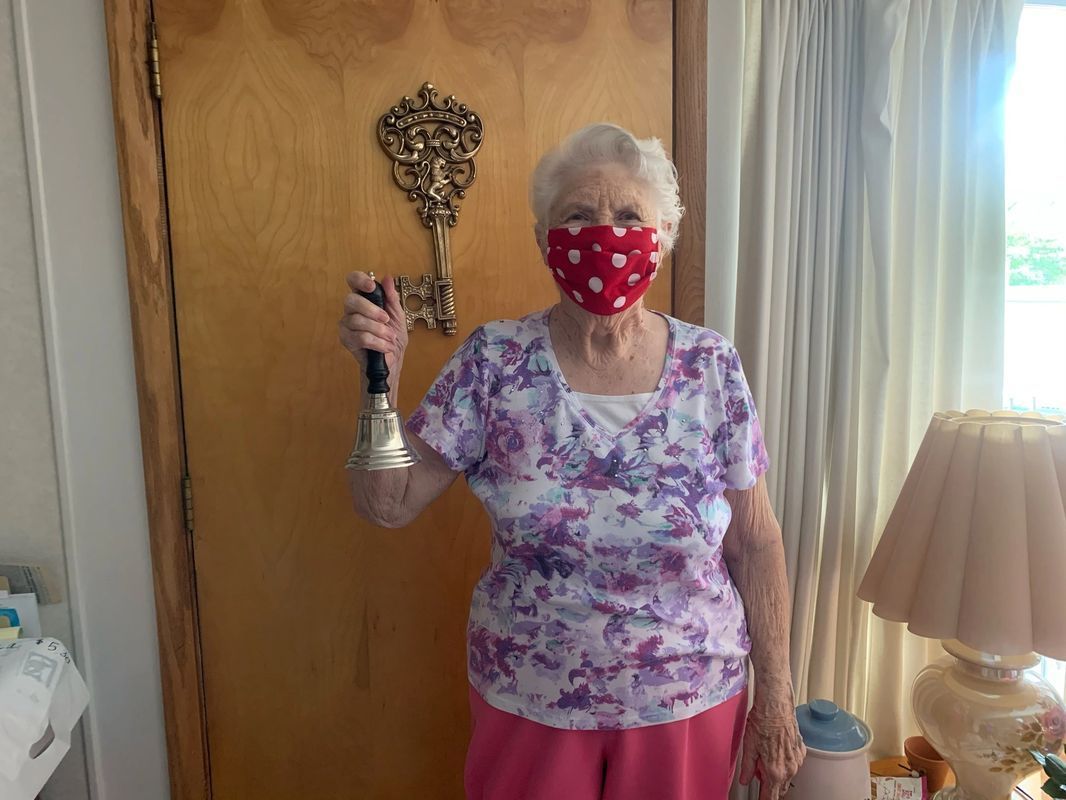 A woman wearing a mask is holding a bell in front of a door.