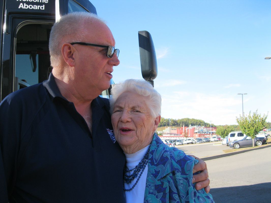 A man and woman are standing in front of a bus that says boarding aboard