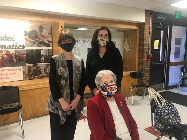 Three women wearing face masks are standing next to each other in a hallway.