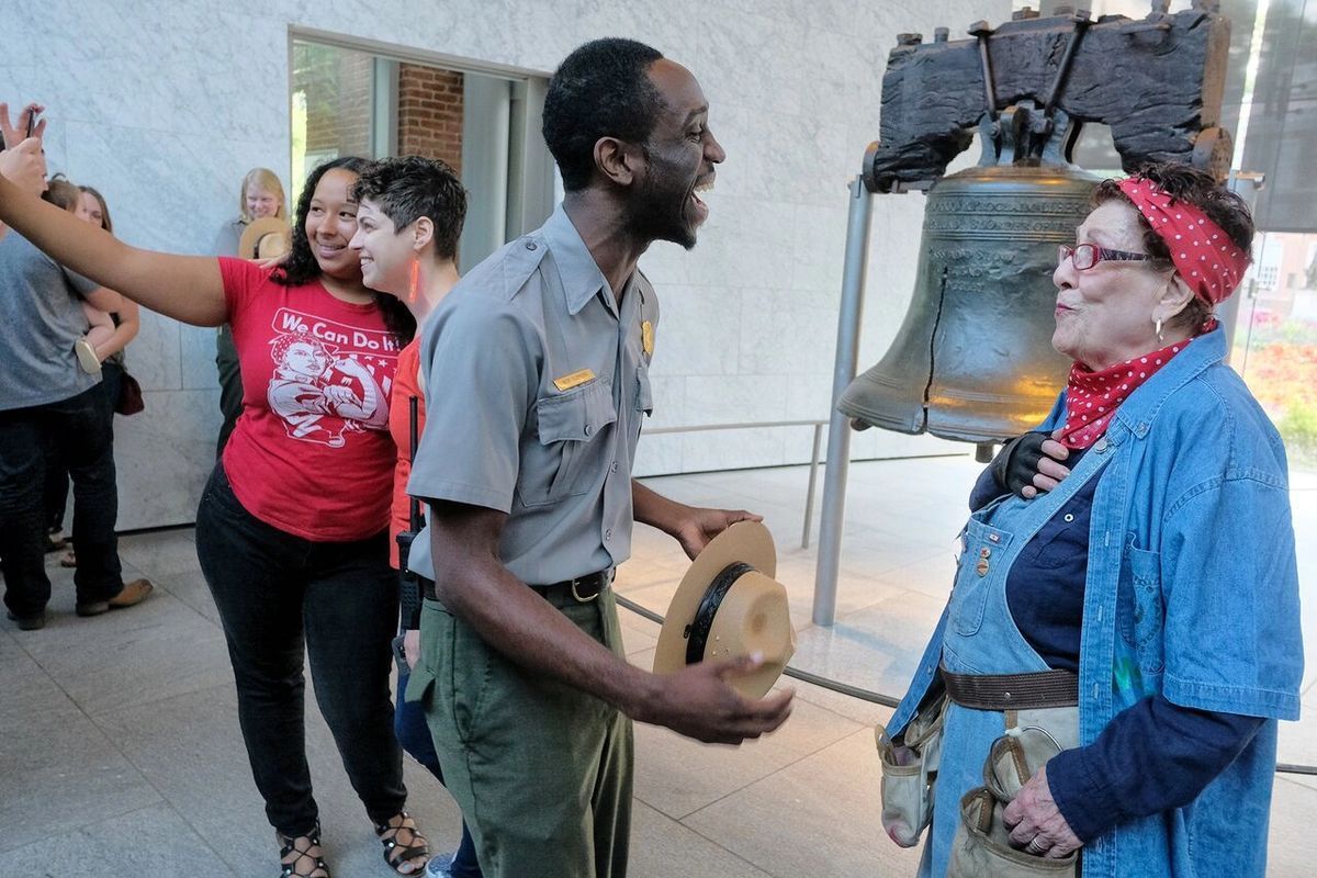 A group of people are standing in front of a liberty bell