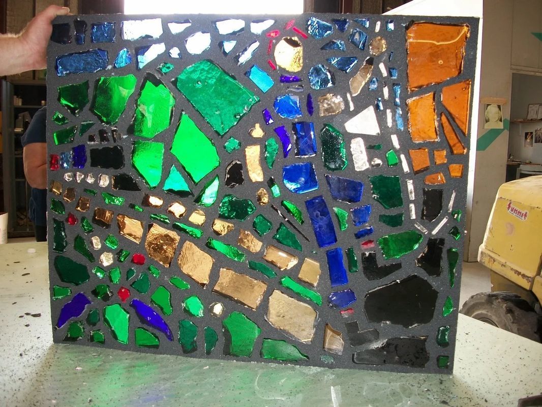 A person is holding a piece of stained glass on a table
