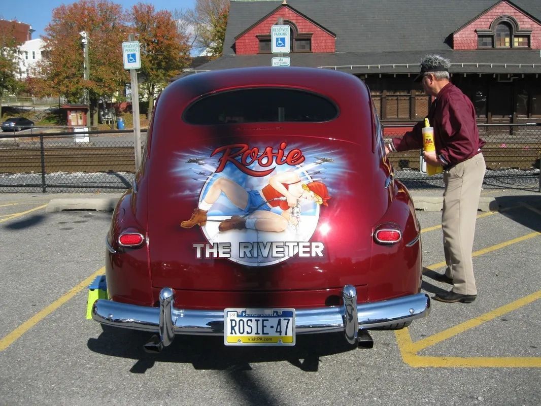 A man standing next to a red car that says the riverder