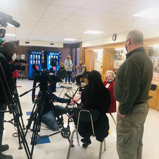 A group of people are gathered in a room with a vending machine in the background