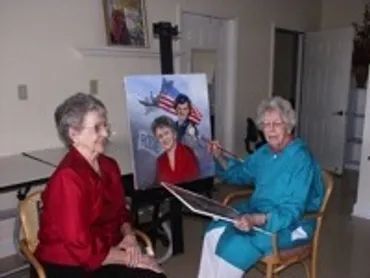 Two women are sitting in front of an easel painting a picture