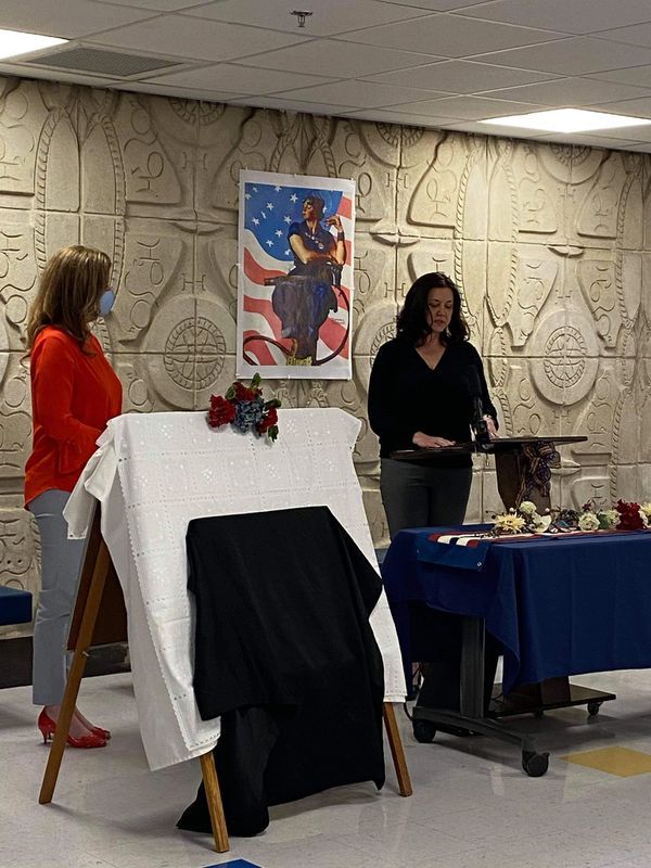 Two women are standing in front of a table with a picture on the wall behind them.