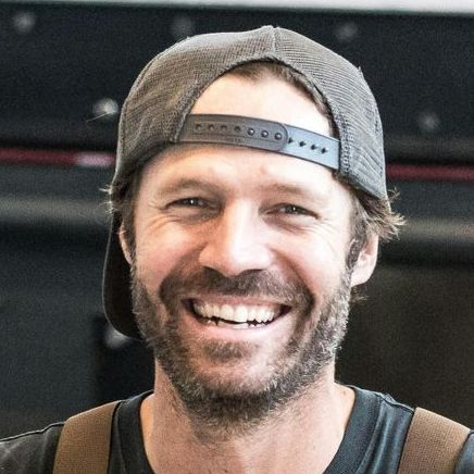 A man with a beard is wearing a baseball cap and smiling.