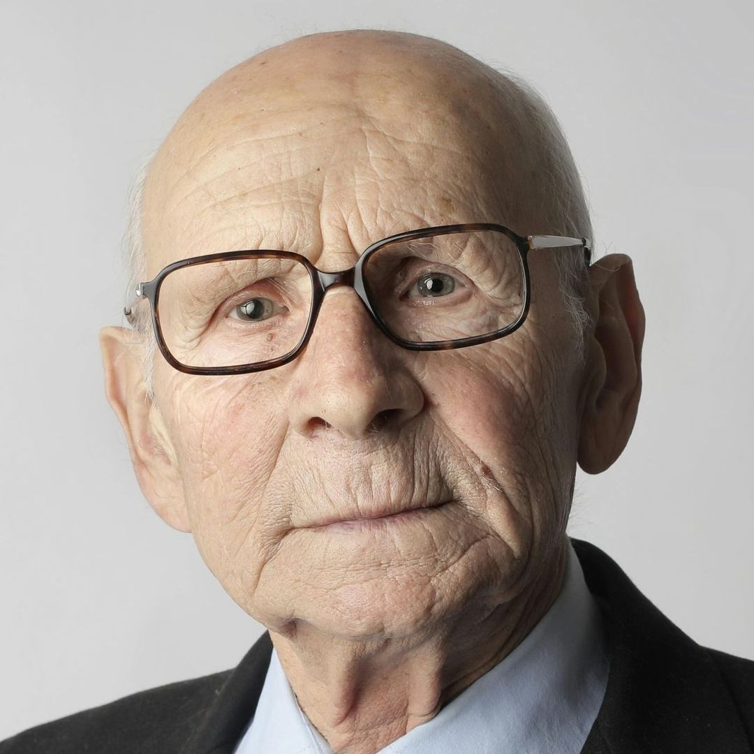 A bald man wearing glasses and a suit is looking at the camera.