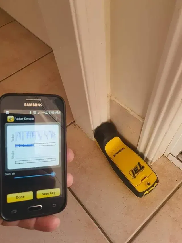 A Person Holding a Cell Phone Next to a Yellow Termite Tracker — Superior Termite & Pest Control in Bundaberg, QLD