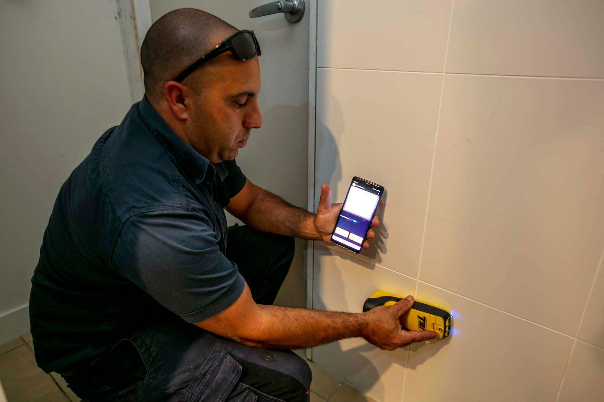 A Man is Using a Cell Phone to Track Termites on a Wall — Superior Termite & Pest Control in Gin Gin, QLD