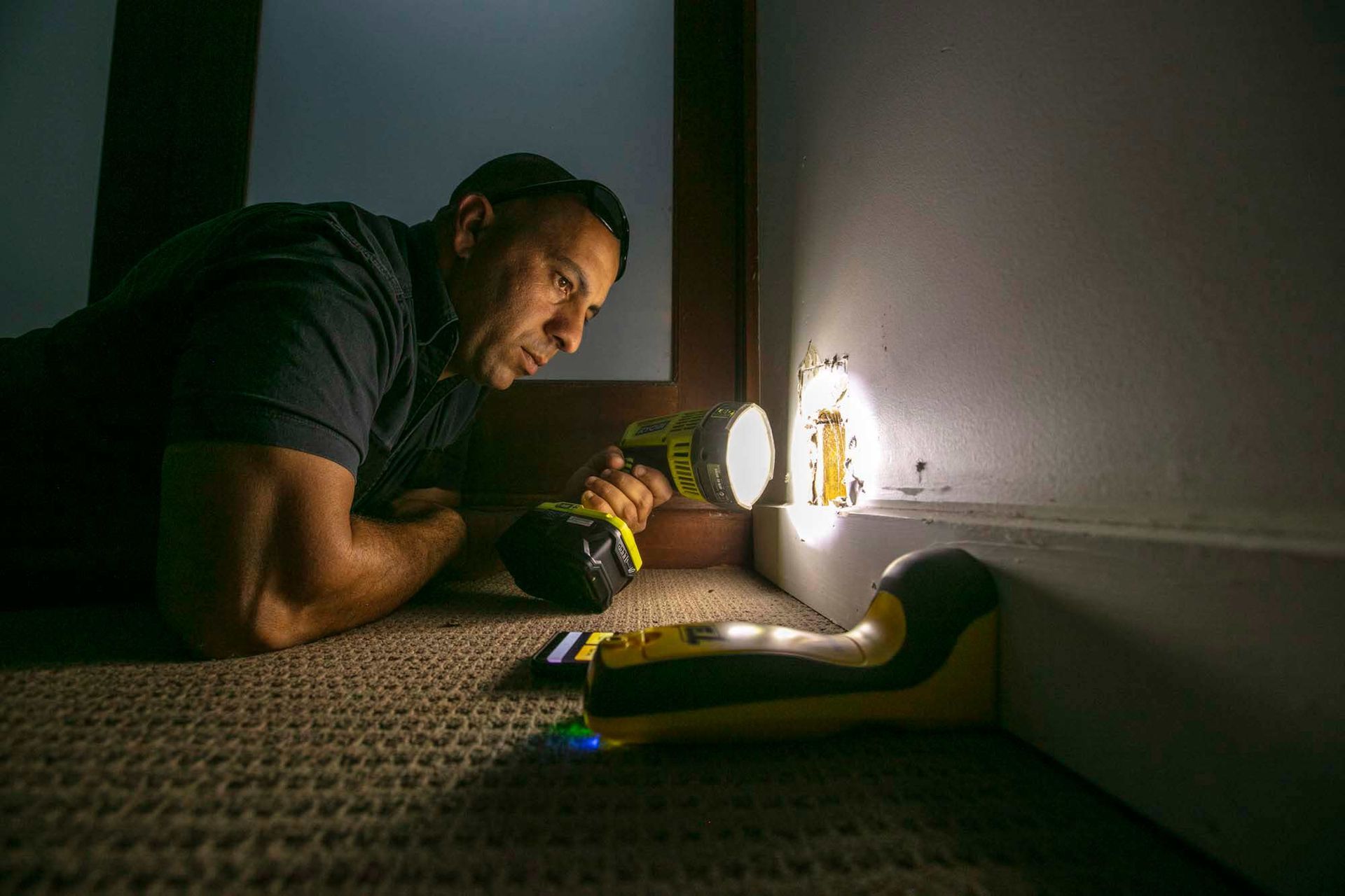 A Man is Looking Through a Hole in a Door With a Flashlight — Superior Termite & Pest Control in Bundaberg, QLD
