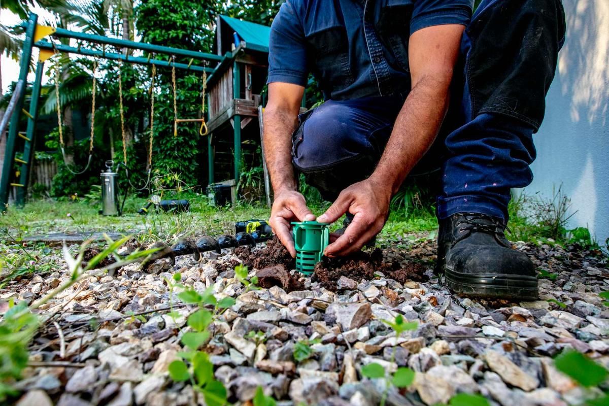 A Man is Installing a Termite Barrier in a Backyard — Superior Termite & Pest Control in Beerwah, QLD
