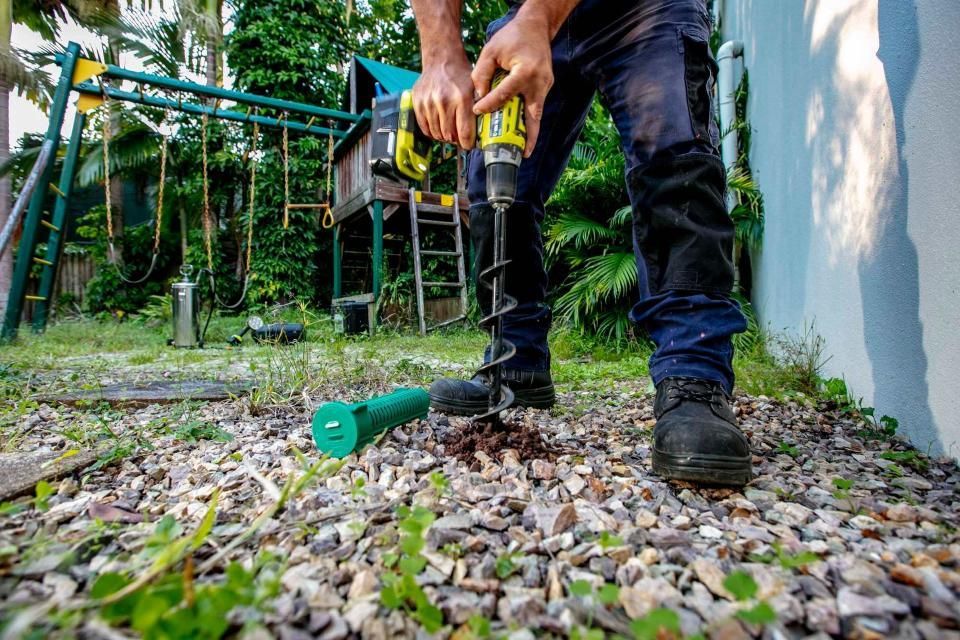 A Man is Drilling a Hole in the Ground — Superior Termite & Pest Control in Tannum Sands, QLD