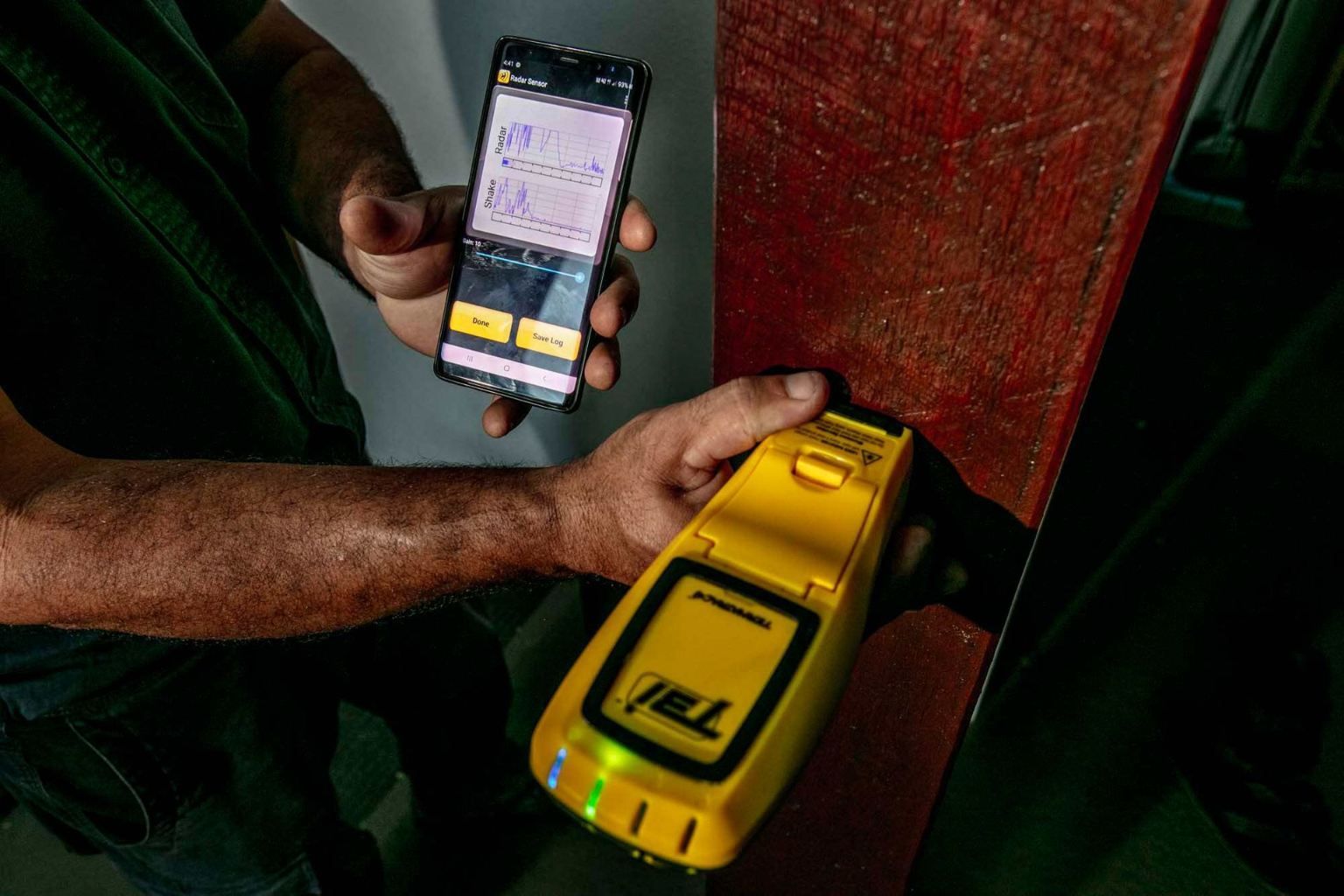 A Man is Holding a Cell Phone and a Yellow Termite Detector — Superior Termite & Pest Control in Bundaberg, QLD