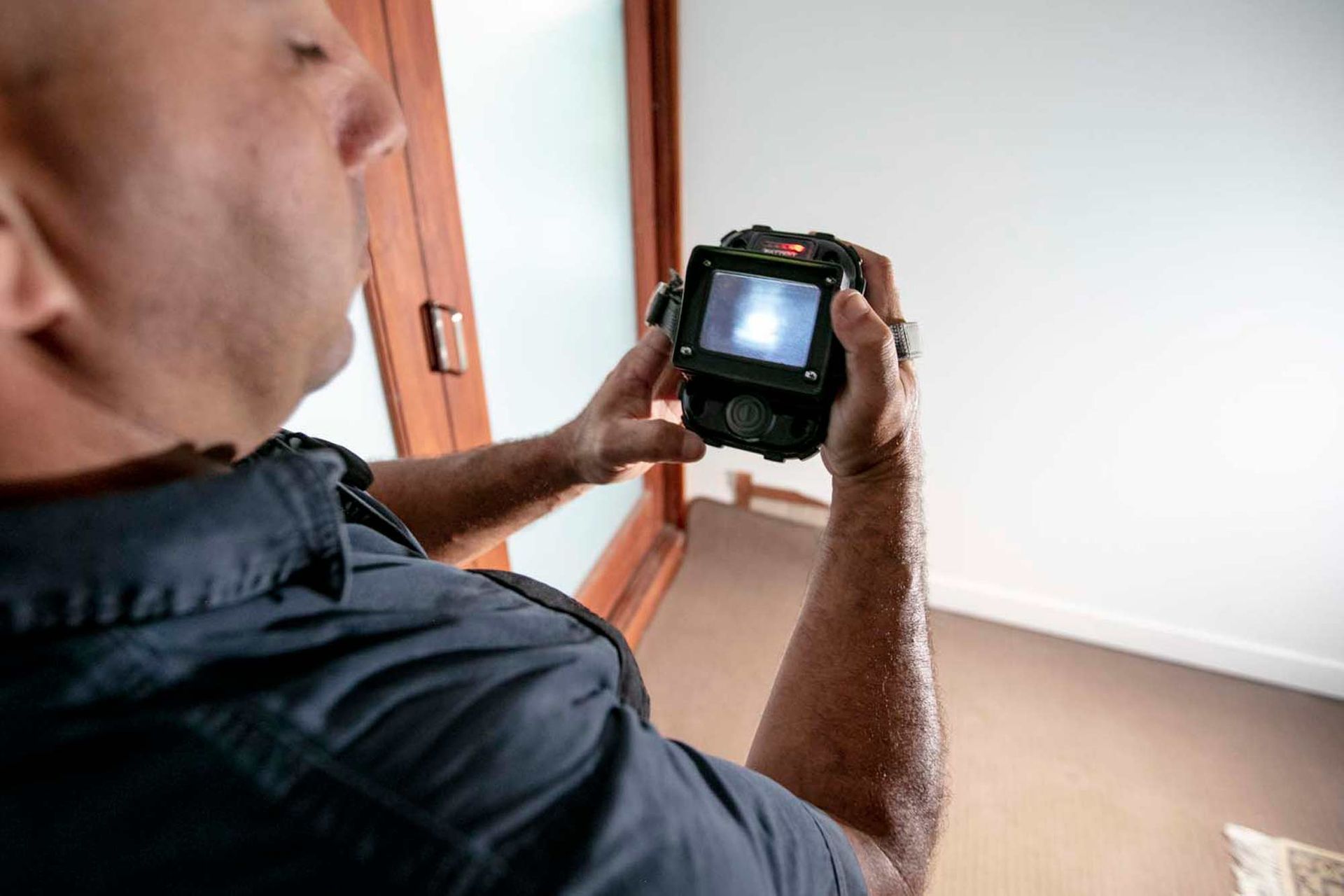 A Man is Holding a Camera in His Hands and Tracking Termites in a Room — Superior Termite & Pest Control in Noosa, QLD