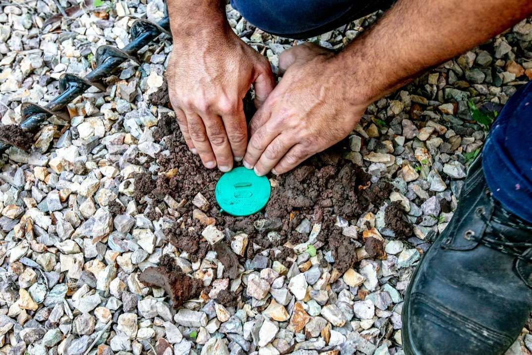 A Man is Kneeling on the Ground Holding a Green Circle in the Dirt — Superior Termite & Pest Control in Nambour, QLD