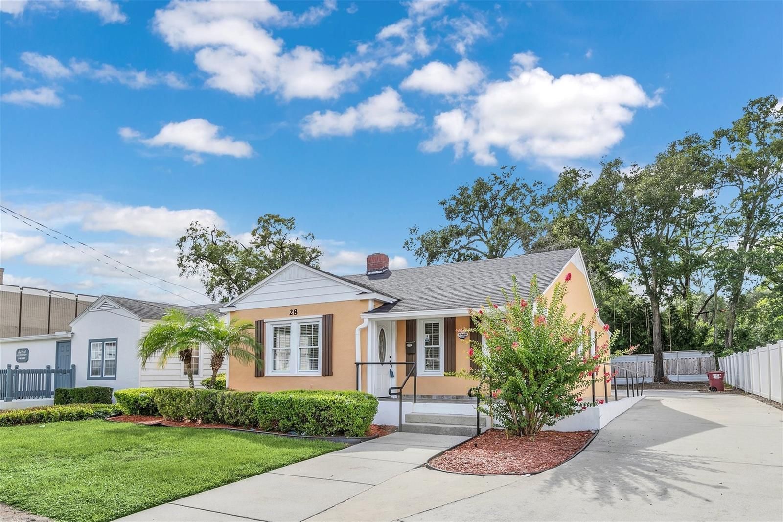 The front of a house with a driveway and trees in the background.