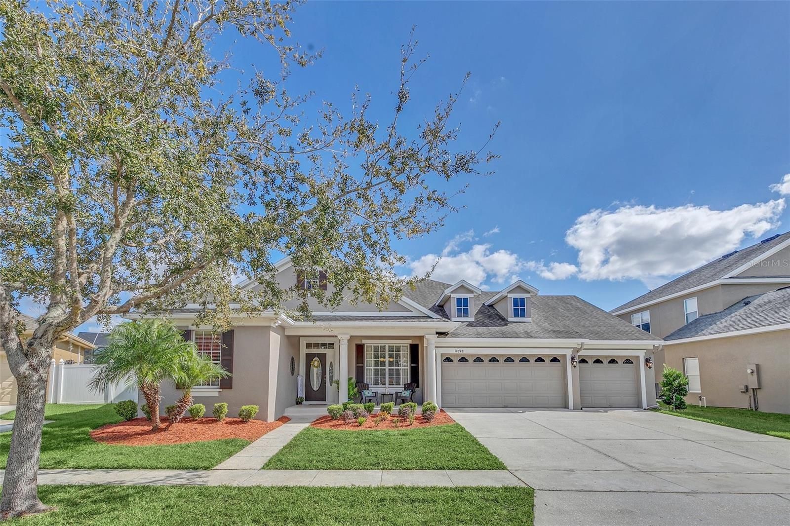A large house with a large driveway and a tree in front of it.