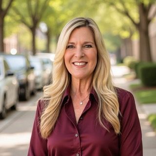 Woman with blonde hair wearing a teal blazer and a white lace top, smiling at the camera.